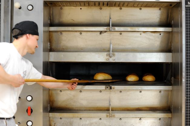 Bäcker holt Brot aus dem Ofen.