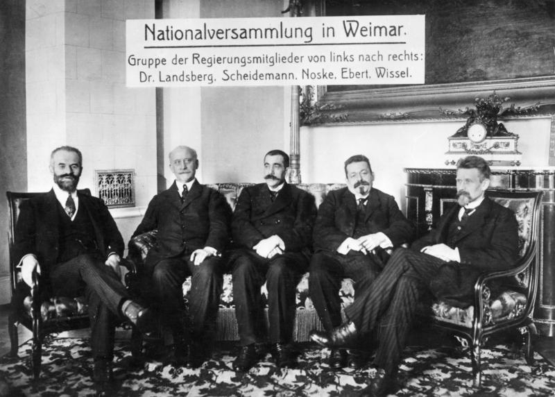 s:222:"Gruppenbild der Regierungsmitglieder der ersten Nationalversammlung am 06.02.1919 in Weimar. V. l. n. r., Otto Landsberg (SPD), Philipp Scheidemann (SPD), Gustav Noske (SPD), Friedrich Ebert (SPD) und Rudolf Wissell (SPD).";