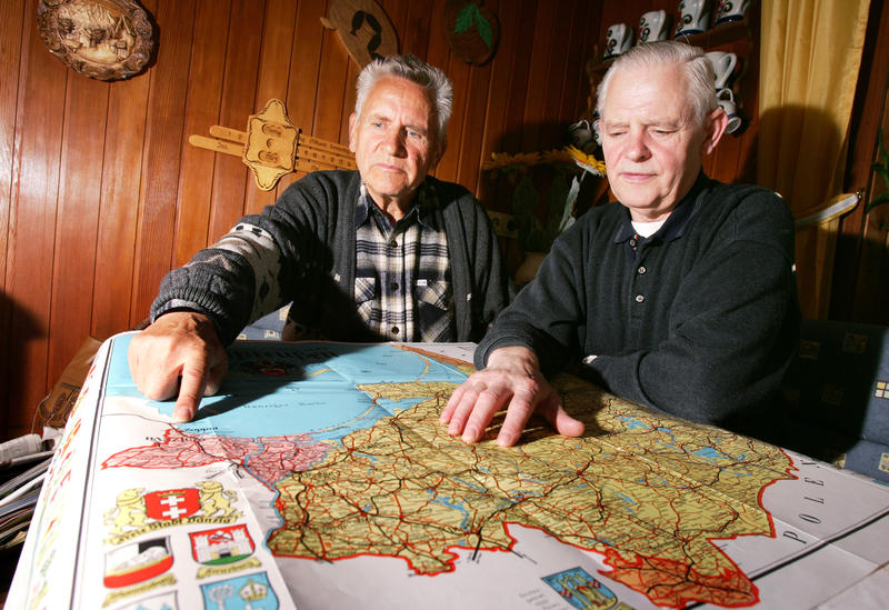 s:194:"Eckhardt (li.) (69) und Gerhard (66) Romahn, Heimatvertriebene aus Ostpreussen, suchen auf einer historischen Ostpreussen-Karte den Weg, den sie als Flüchtlinge nehmen mussten (Foto undatiert).";