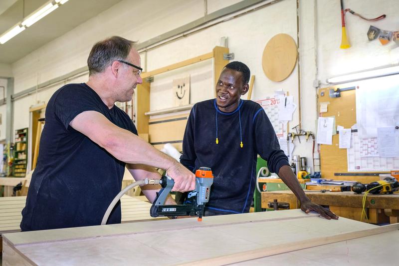 s:181:"Moussa Soukouna, Fluechtling aus Mali, und Ausbildungsleiter Olaf Fredriksen, am 03.07.2018 in der Tischlerwerkstatt des Opernhauses Hannover, wo Soukouna ein Praktikum absolviert. ";