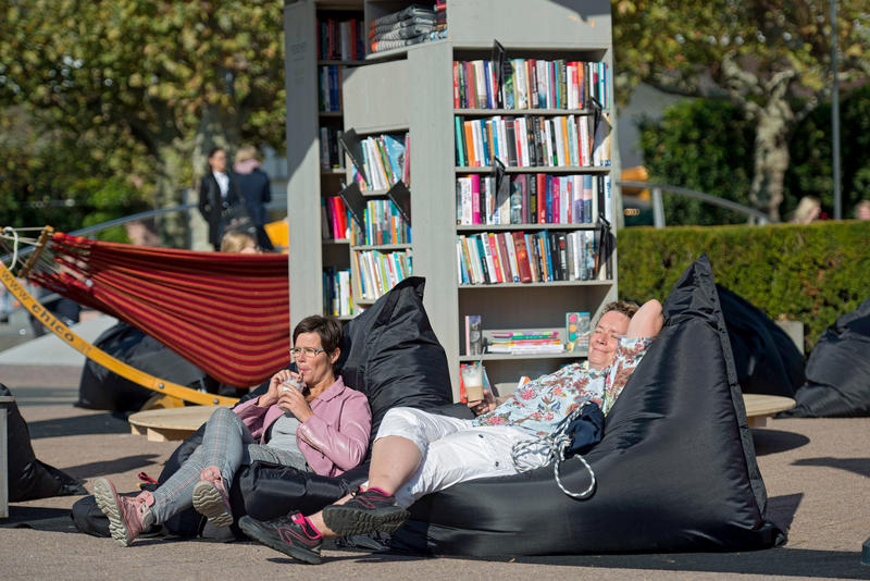s:129:"Die Frankfurter Buchmesse hat am 10.10.18 ihre Tore fuer den Fachhandel geoeffnet (Foto: Besucher erholen sich im Aussenbereich).";