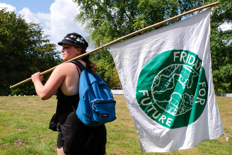 s:150:"ine Teilnehmerin vom "Fridays for Future"-Sommerkongress traegt am 01.08.19 im Dortmunder Revierpark Wischlinghausen eine "Fridays for Future"-Fahne. ";