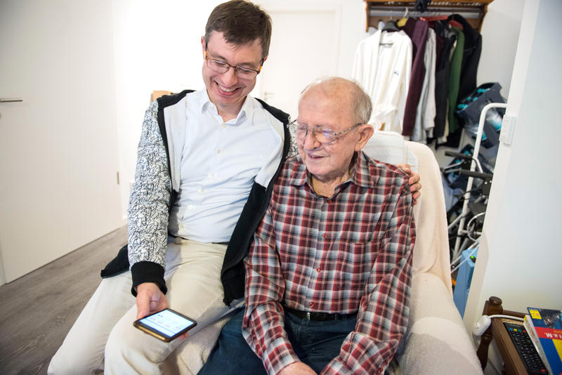 s:86:"Jörg Ehm erklärt seinem Vater Bruno, wie er mit dem Smartphone "Alexa" steuern kann.";