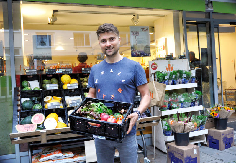 s:73:"Daniel Nagy mit einer Gemüsekiste vor einem Lebesmittelladen in München";