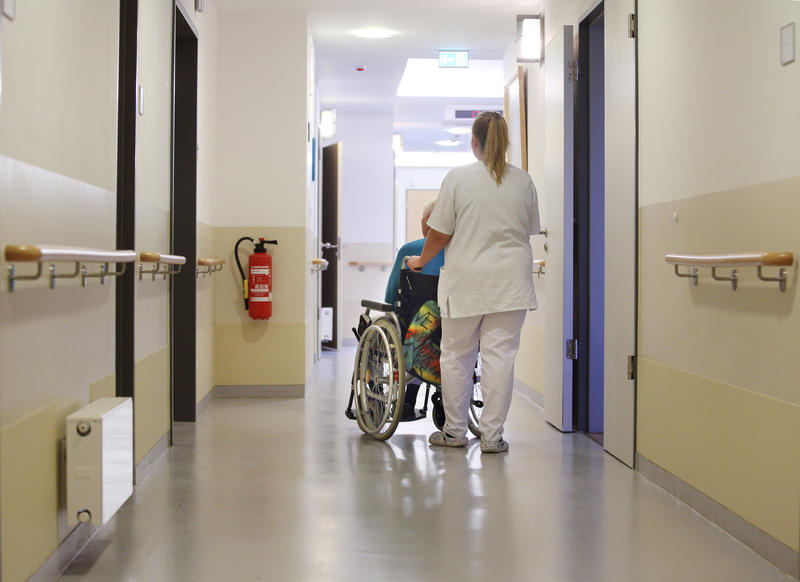 s:48:"Pflegekraft schiebt Heimbewohnerin im Rollstuhl.";