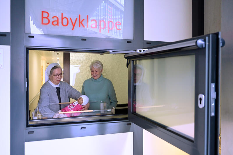 s:119:"Schwester Annette Biecker (l.) und Marion Meister mit einer Puppe an der Babyklappe am St. Vinzenz-Krankenhaus in Hanau";