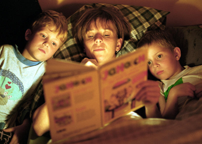 s:63:"Mutter liest ihren Kindern aus einem Kinderbuch von Janosch vor";