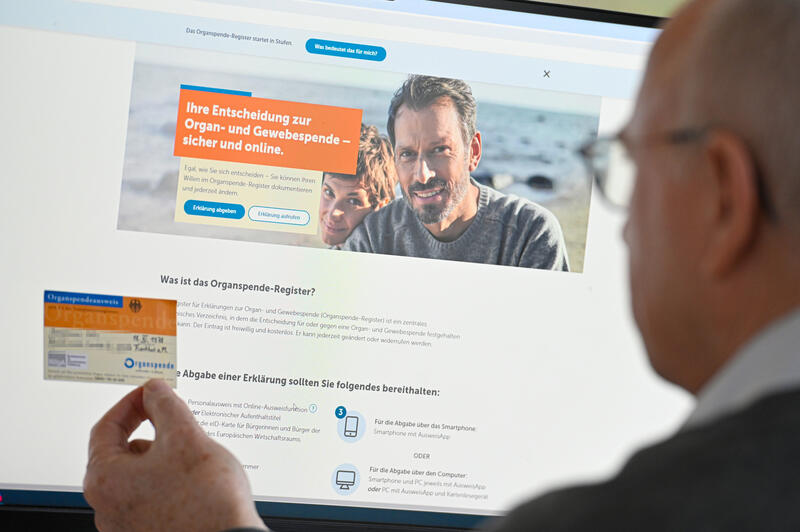 s:136:"Die Internetseite "www.organspende-register.de" auf einem Bildschirm und ein Organspendeausweis in der Hand eines Anwenders (Themenfoto)";