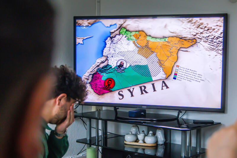 s:87:"Syrische Flüchtlinge verfolgen die Geschehnisse in ihrer Heimat (Foto vom 15.12.2024).";
