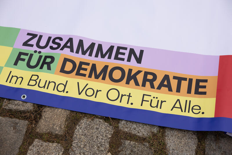 s:50:"Ein Banner wirbt vor einer Kirche für Demokratie.";