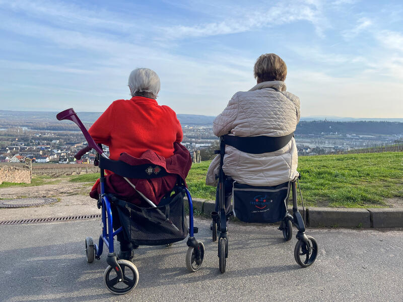 s:45:"Zwei Rentnerinnen sitzend auf ihrem Rollator.";