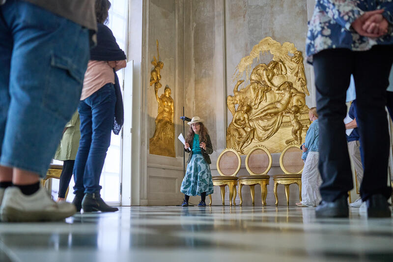 s:91:"Lila Riedel (Mitte) bei einer Führung im Schloss Neue Kammern im Park Sanssouci in Potsdam";