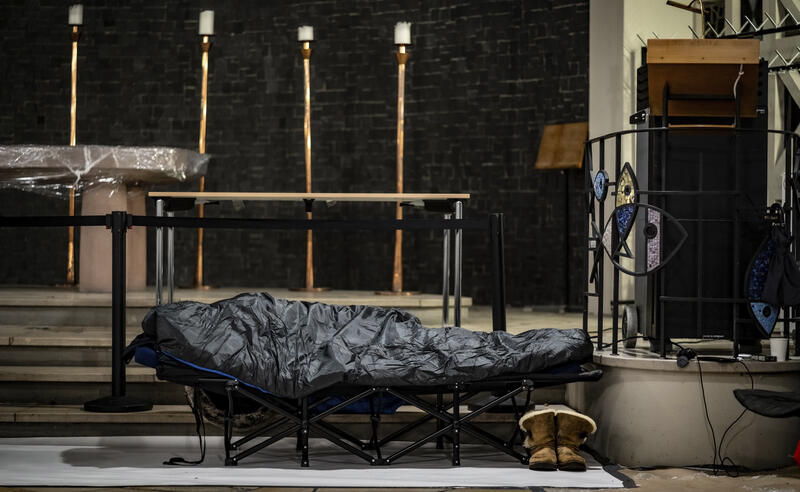 s:83:"Ein Mann in seinem Schlafsack auf einem Feldbett in der Weißfrauen-Diakoniekirche.";