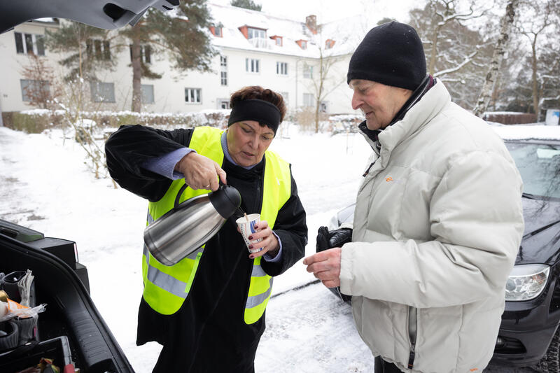 s:119:"Mitglieder der Evangelischen Emmaus-Gemeinde in Zehlendorf schenken am 6. Januar heiße Getränke in Thermoskannen aus.";
