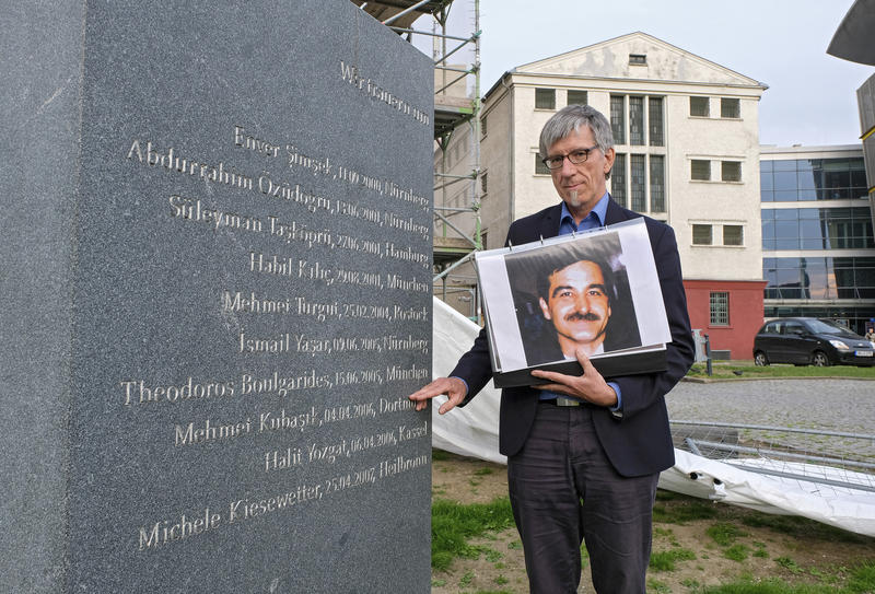 s:152:"Der evangelische Pfarrer Friedrich Stiller mit einem Foto des Dortmunder NSU-Opfers Mehmet Kubasik am Mahnmahl für die Opfer der NSU-Morde (Archivfoto)";