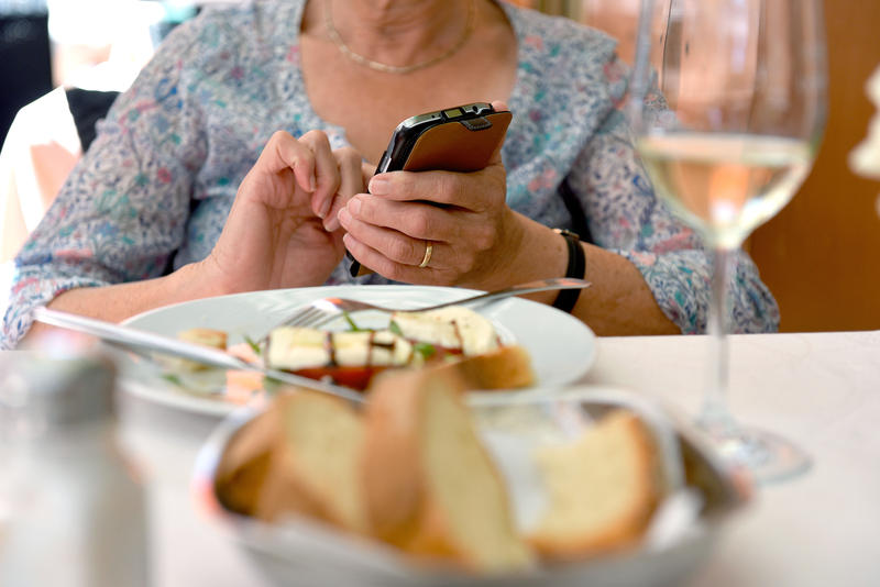 s:83:"Eine Frau hält während des Essens in einem Restaurant ein Smartphone in der Hand.";