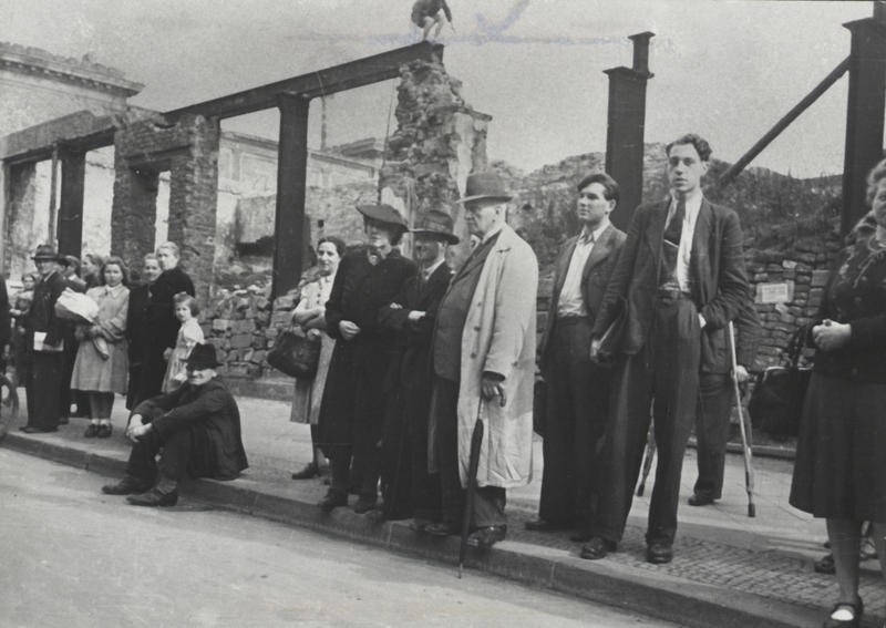 s:172:"Menschen am Straßenrand beobachten am 2. Oktober 1946 die Eröffnung des ersten nordrhein-westfälischen Landtags im Opernhaus, im Hintergrund die Trümmer der Kunsthalle.";